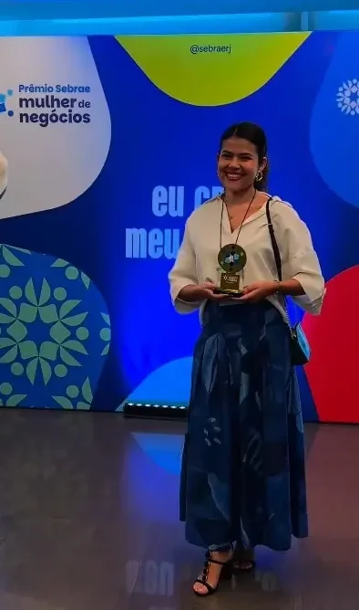 Luize Freire em pé, sorrindo, segurando o troféu do Prêmio Sebrae Mulher de Negócios
