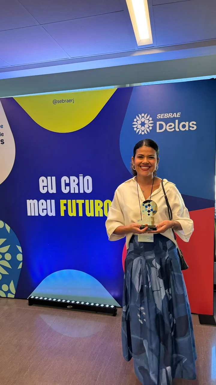 Luize Freire em pé, sorrindo, segurando o troféu do Prêmio Sebrae Mulher de Negócios